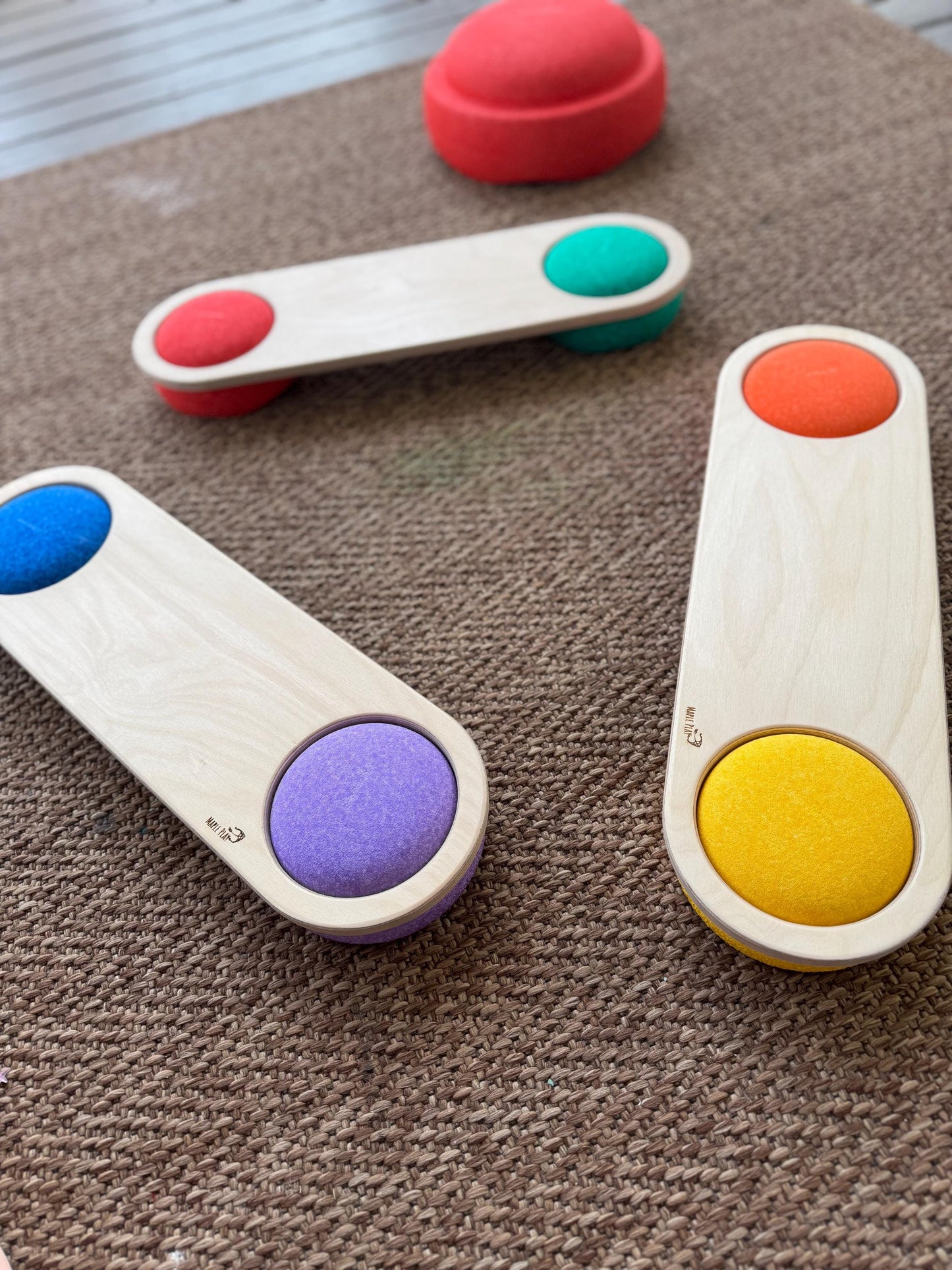 A set of three wooden balance boards with colorful circular inserts on each end, placed on a brown surface.