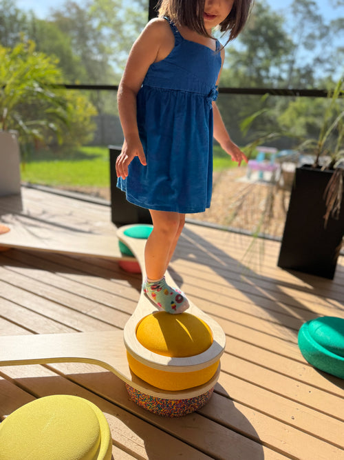 Toddler standing on wooden balance board with Stapelstein stepping stones