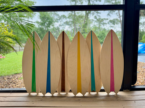 Set of six wooden surfboard-shaped decorations with colorful stripes on a wooden surface.