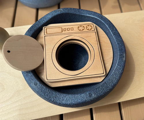A wooden lid in a form of a washer with the door open inside  Stapelstein stepping stone 